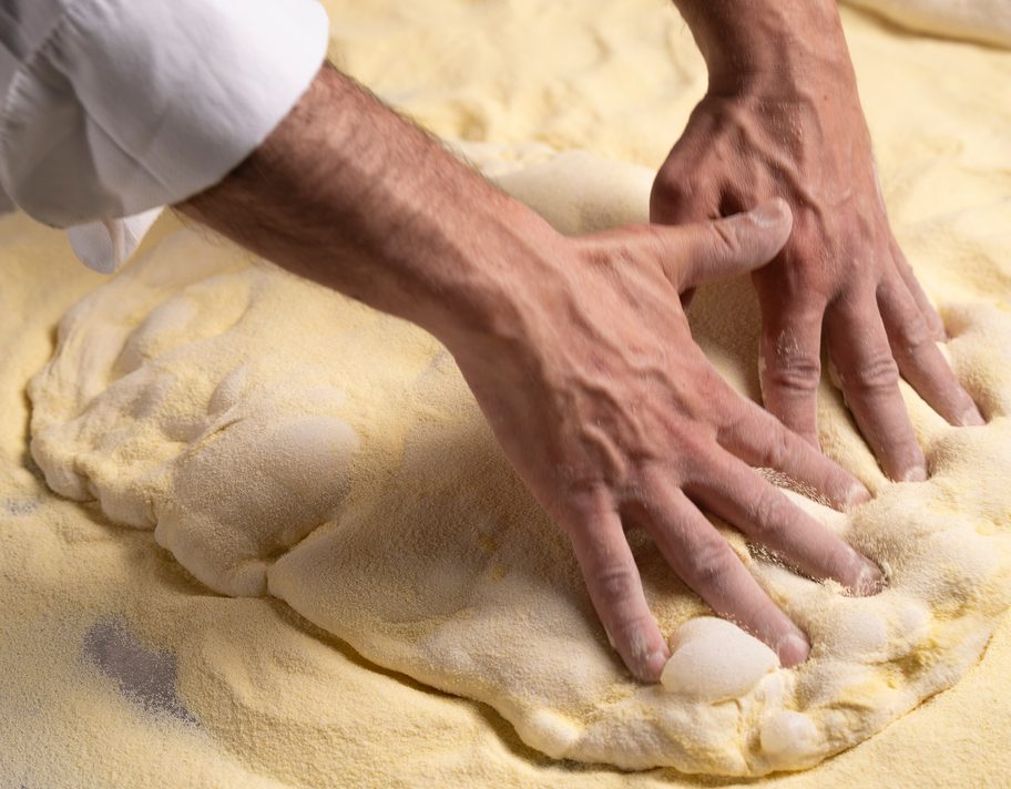 Mani che lavorano l’impasto sul banco infarinato.
